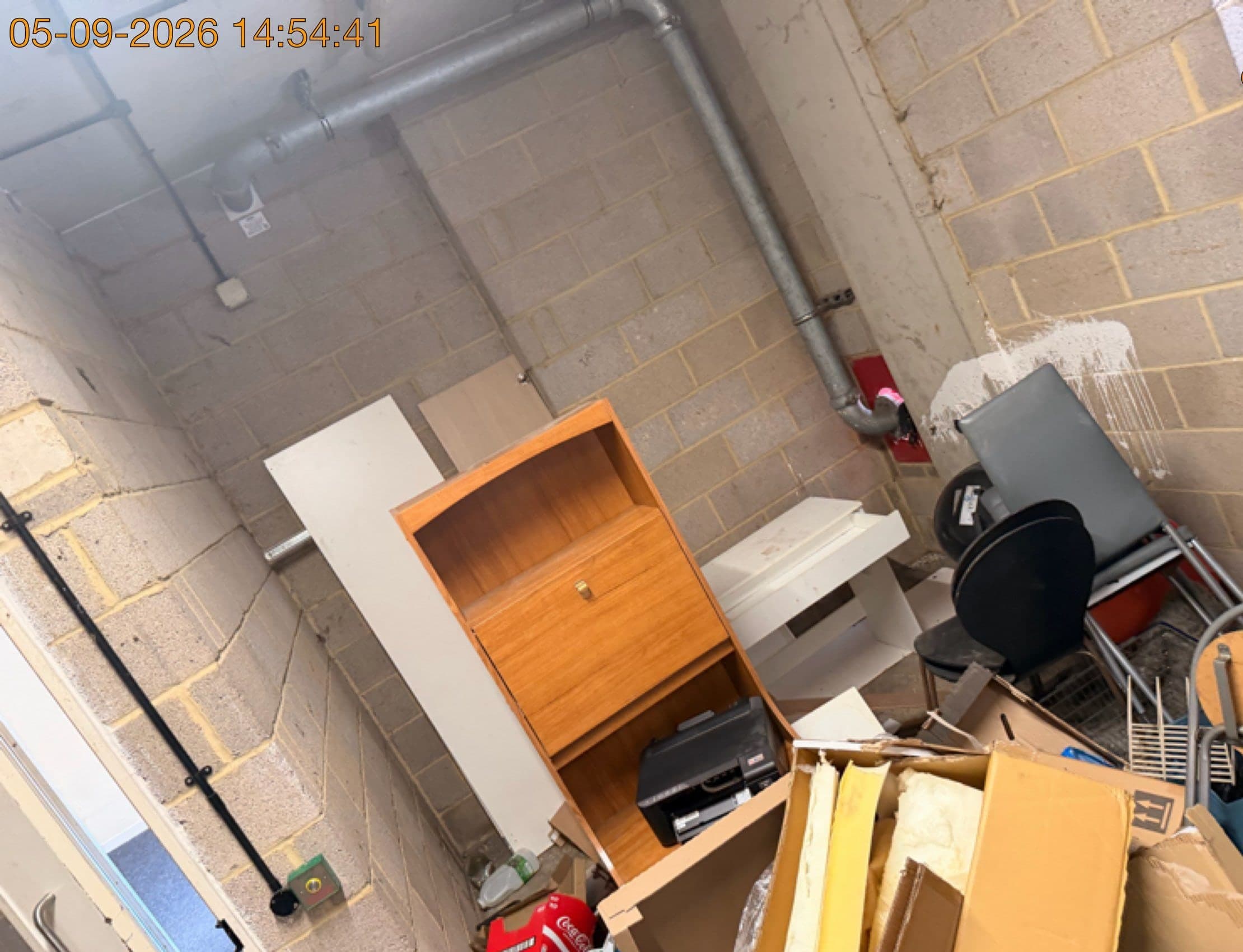 Fly-tipped bureau, office chair, printer and boxes of clutter dumped in a communal bin store before clearance