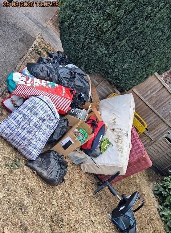 Pile of household waste on a lawn including bin bags, boxes, an old mattress and an exercise bike