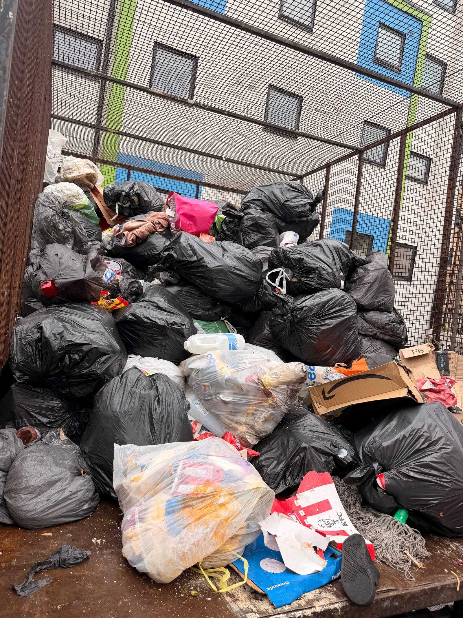 Large pile of black bin bags and household waste inside a caged bin store