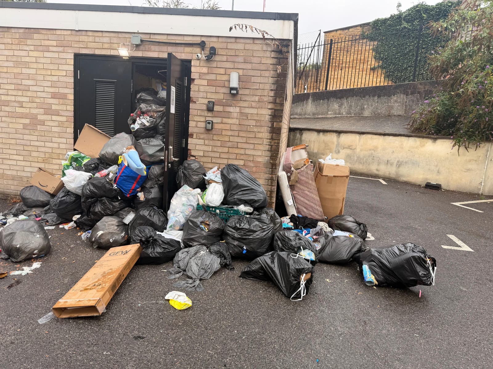 Overflowing communal bin store packed with black bin bags and cardboard before clearance