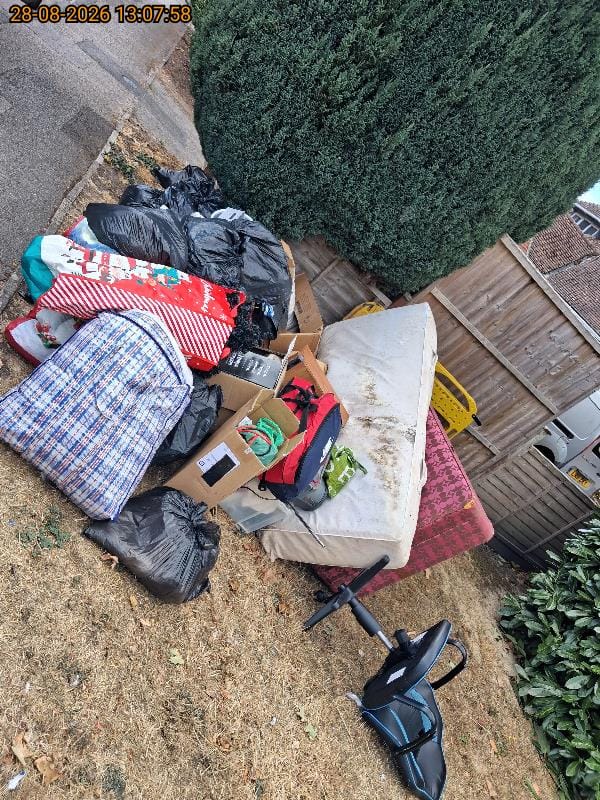 Pile of household waste on a lawn including bin bags, boxes, an old mattress and an exercise bike