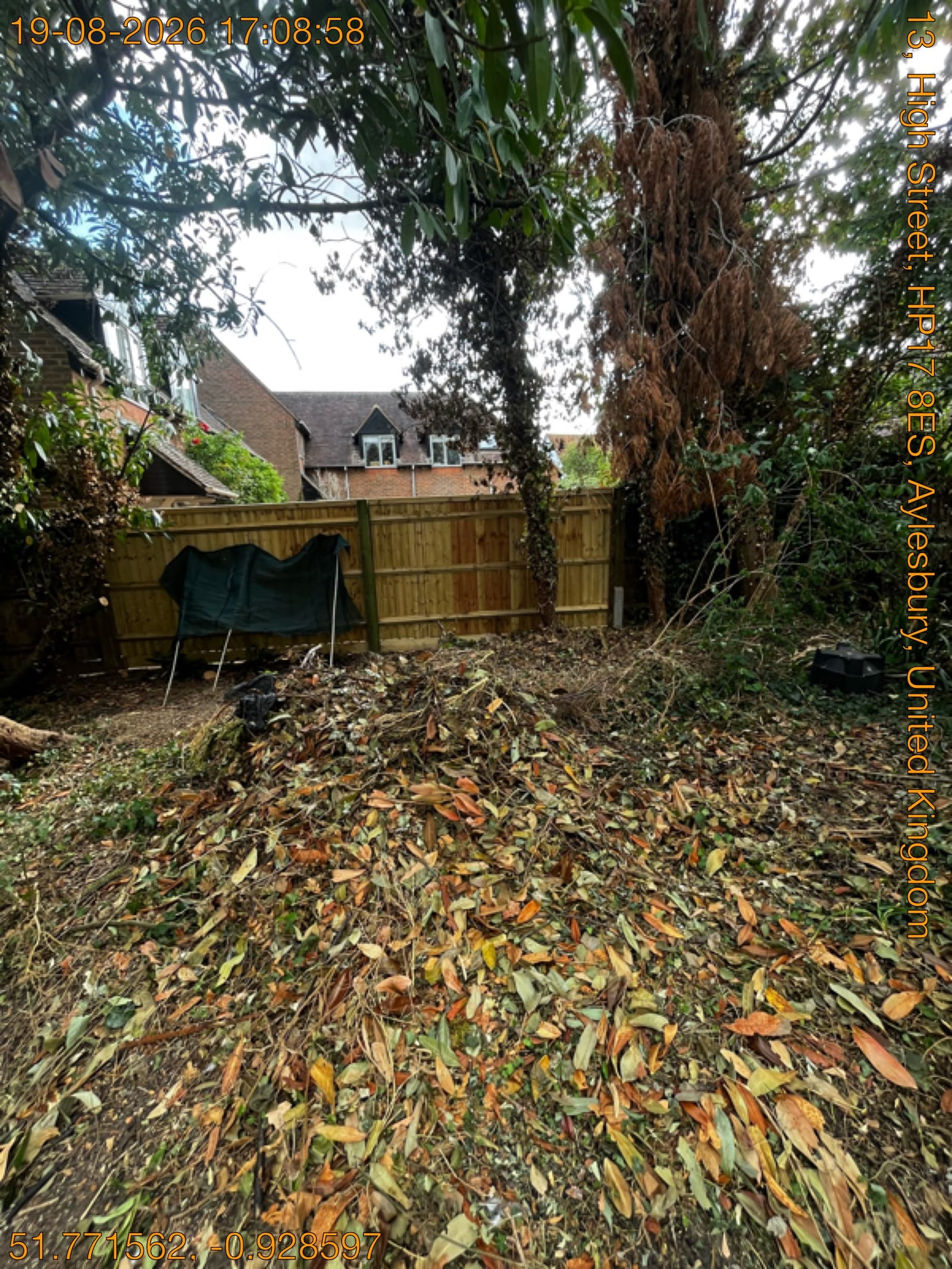 Garden strewn with fallen leaves and cut vegetation beside new fence panels ready for clearance